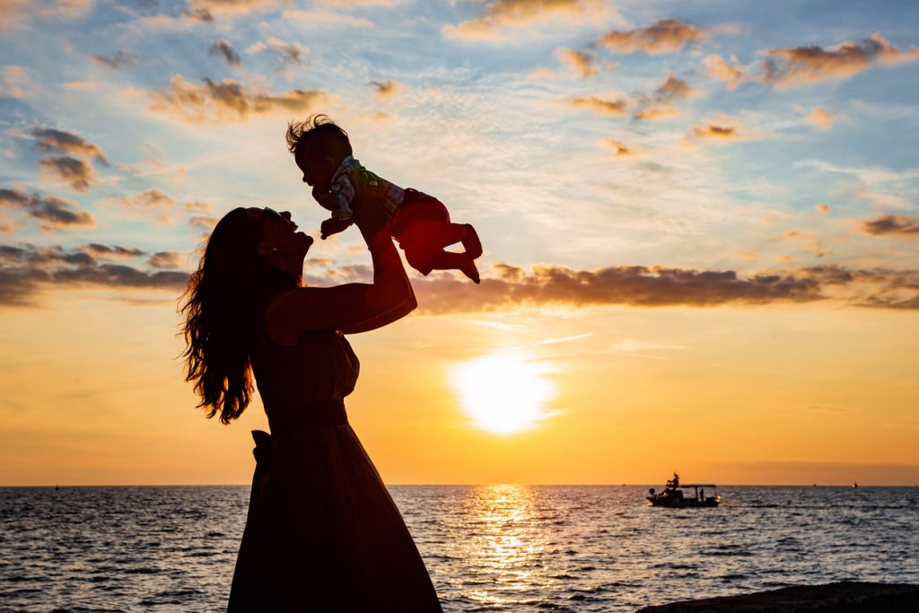 Mother enjoying the sun at the beach with her baby boy in Rovinj near a rent-a-boat